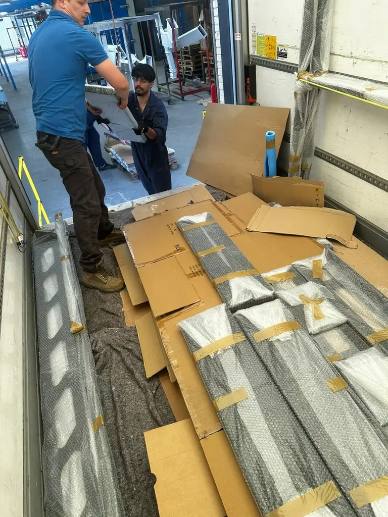 Two 2FAST movers handling cardboard and bubble-wrapped panels in the back of a van